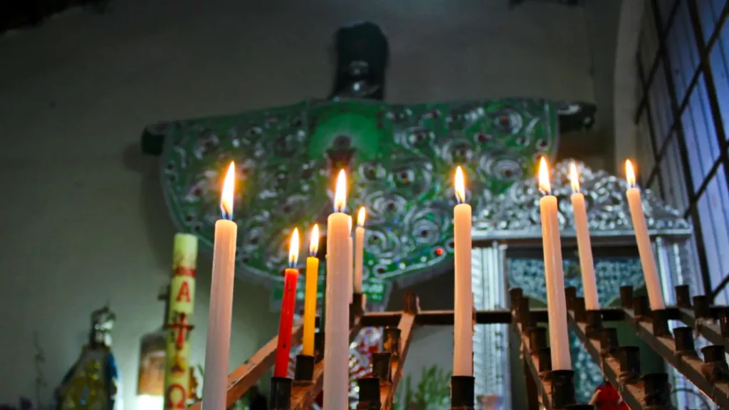 Lit candles and religious icon in Andean chapel during Cruz Velacuy